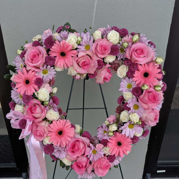 Heart-shaped floral wreath with pink roses and daisies on a stand