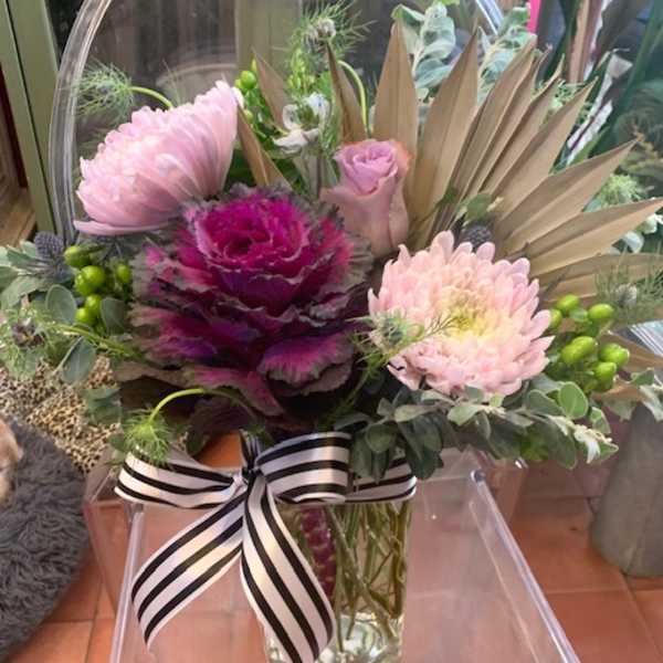 Pink and magenta floral arrangement in a clear glass vase with a striped ribbon