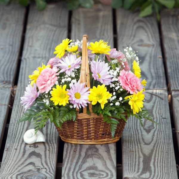 Basket of yellow, pink, and lavender flowers on a wooden deck