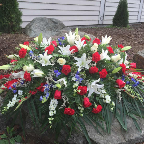 Large funeral spray with white lilies, red roses, and blue flowers