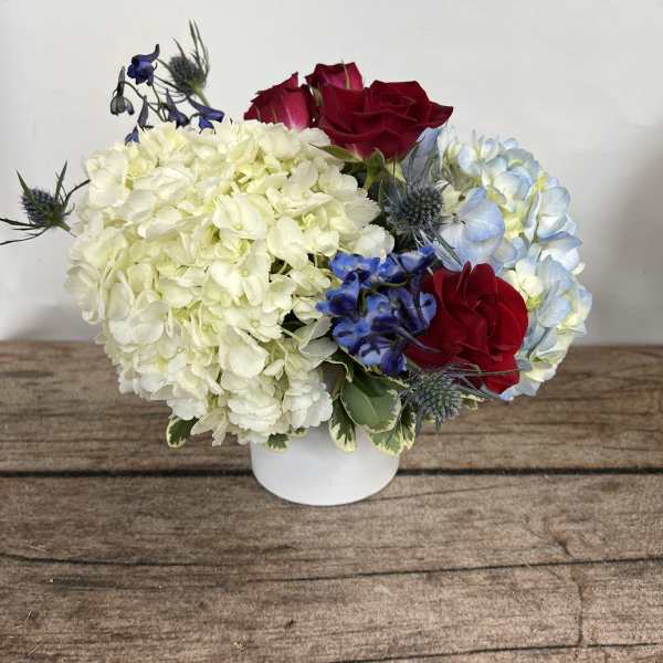 Compact bouquet of white hydrangeas, red roses, and blue flowers in a white vase