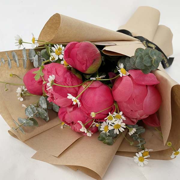 Bouquet of bright pink peonies with small white daisies in brown paper