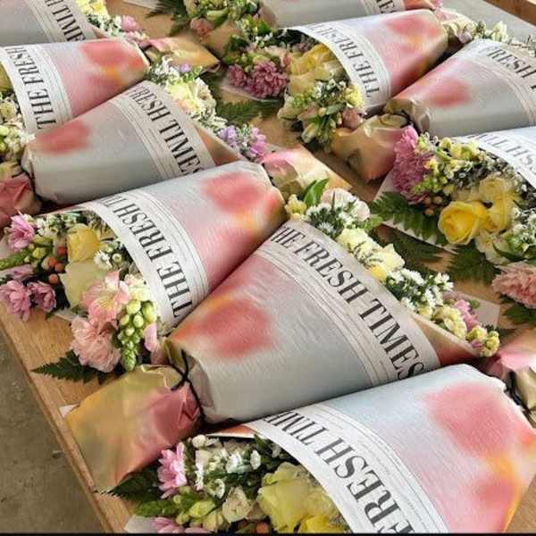 Multiple pastel-wrapped mixed flower bouquets with yellow roses and pink blooms on a wooden table