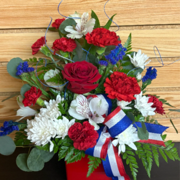 Red, white, and blue floral arrangement in a red container with ribbon