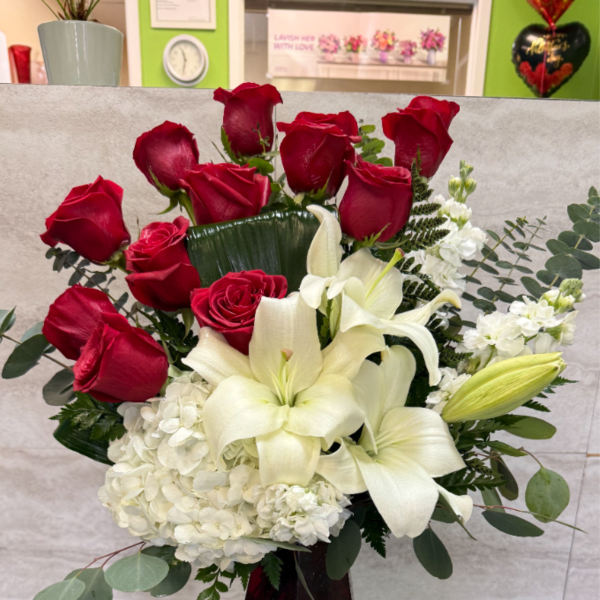 Tall arrangement of red roses, white lilies, and white hydrangeas in a red glass vase