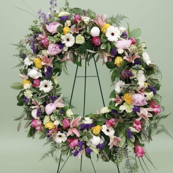 Large floral wreath on a black stand with pink, white, yellow, and purple blooms