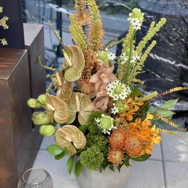 Tall mixed floral arrangement in a gray vase with orange, green, and peach blooms