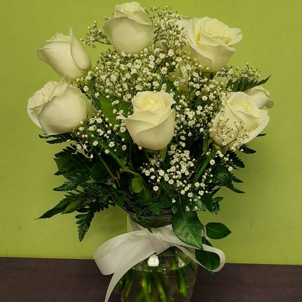White roses and baby's breath in a glass vase with a white ribbon