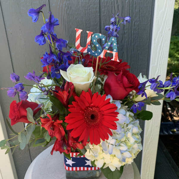 Red, white, and blue flower arrangement in a glass vase with a USA pick