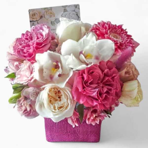 Compact arrangement of pink and white roses, orchids, and mixed blooms in a pink square vase with a card.