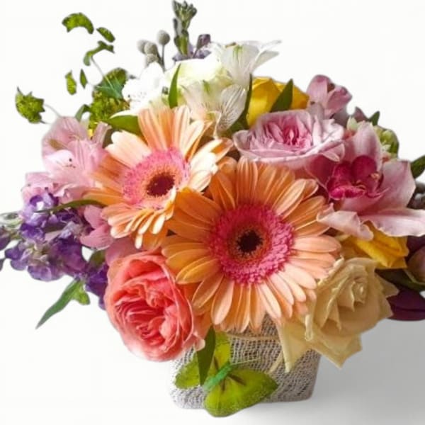 Colorful bouquet of peach gerbera daisies, roses, and mixed blooms in a small textured container