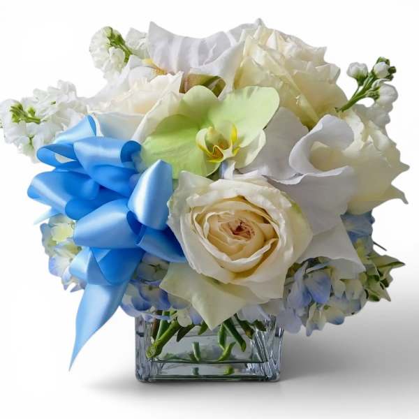 White floral arrangement with a blue ribbon in a square glass vase