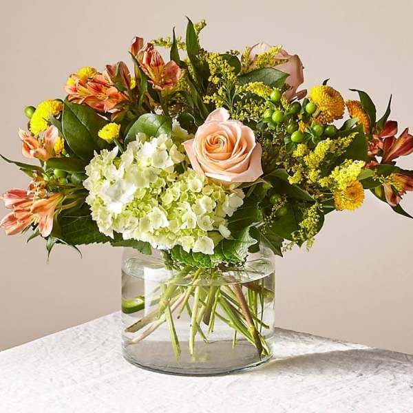 Mixed bouquet of peach roses, white hydrangea, and yellow flowers in a glass vase