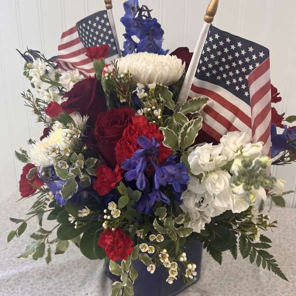 Red, white, and blue floral arrangement with two small American flags in a vase