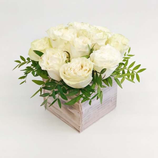 White roses arranged in a square wooden box with green foliage