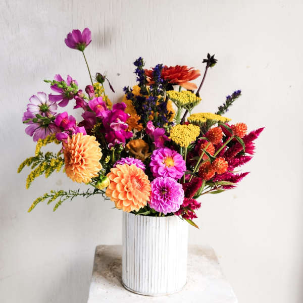 Mixed bouquet of orange, pink, yellow, and purple flowers in a white vase