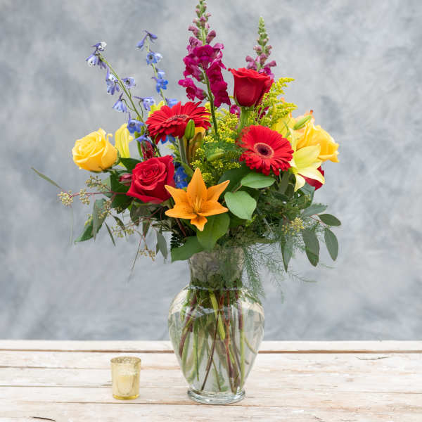Mixed bouquet of roses, lilies, and gerbera daisies in a glass vase