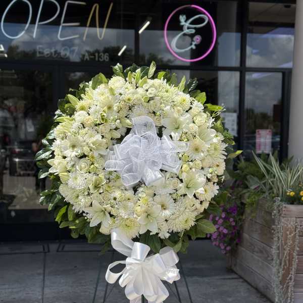 White funeral wreath on a stand with a ribbon bow