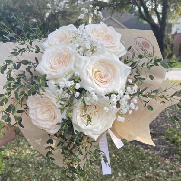 Bouquet of white roses with baby's breath and greenery in kraft paper