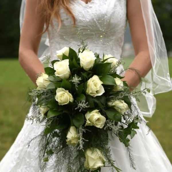 Bride holding a cascading bouquet of white roses with trailing greenery