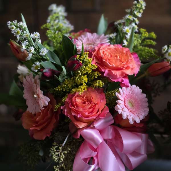 Pink and coral roses with daisies in a white vase, tied with a pink ribbon