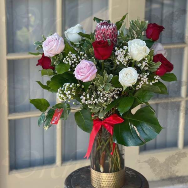 Bouquet of red, white, and pink roses in a glass vase with a red ribbon