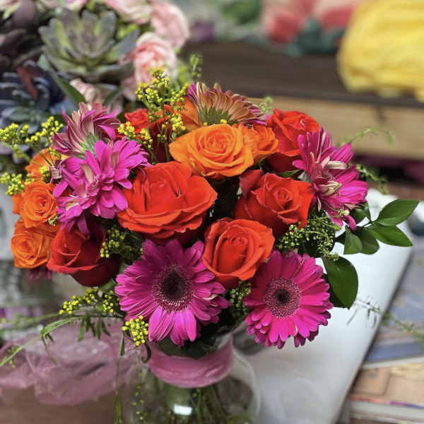 Bouquet of orange and red roses with pink daisies in a glass vase
