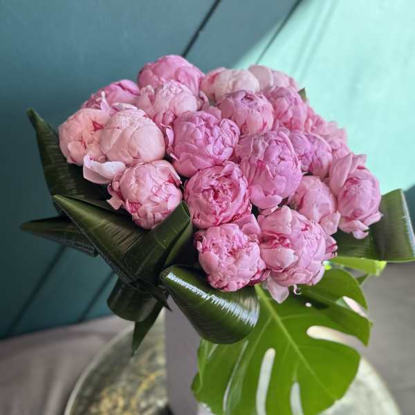 Pink peonies arranged in a white box with tropical leaves