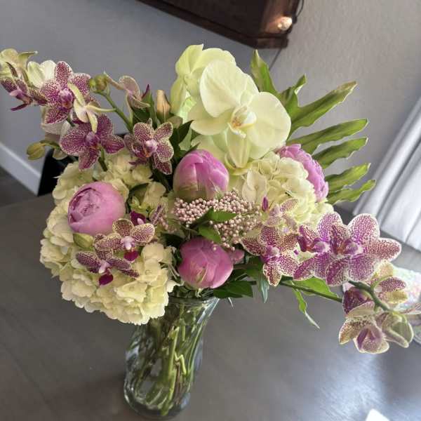 Bouquet of pink peonies, white hydrangeas, and spotted orchids in a glass vase