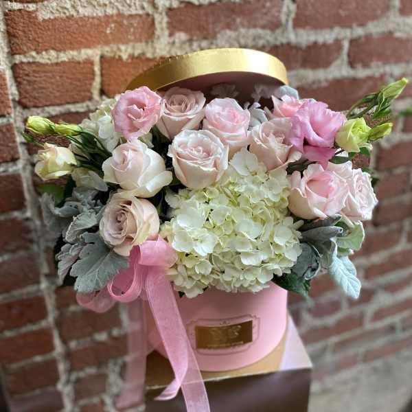 Pink and white roses arranged in a round hatbox with a ribbon