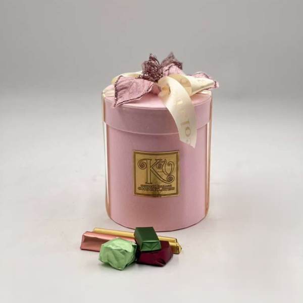 Pink gift box with ribbon and assorted chocolates in front
