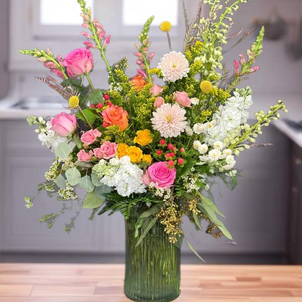 Mixed pink, white, and yellow flowers in a tall green glass vase