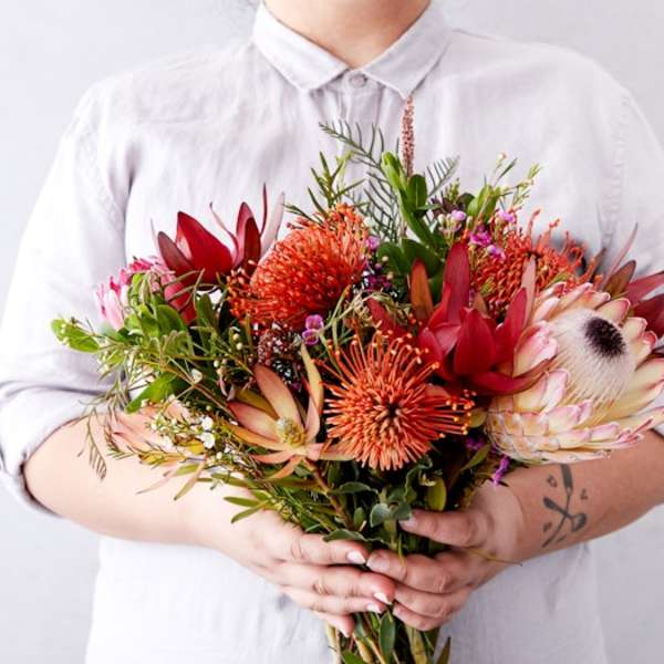 Person holding a bouquet of red and orange tropical flowers