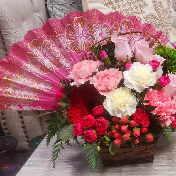 Pink floral arrangement in a basket with a decorative fan backdrop