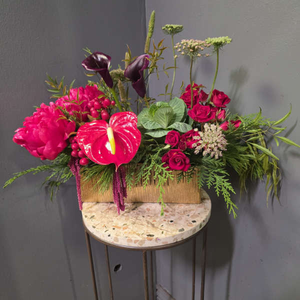 Bright pink floral arrangement with roses, calla lilies, and anthurium in a gold box