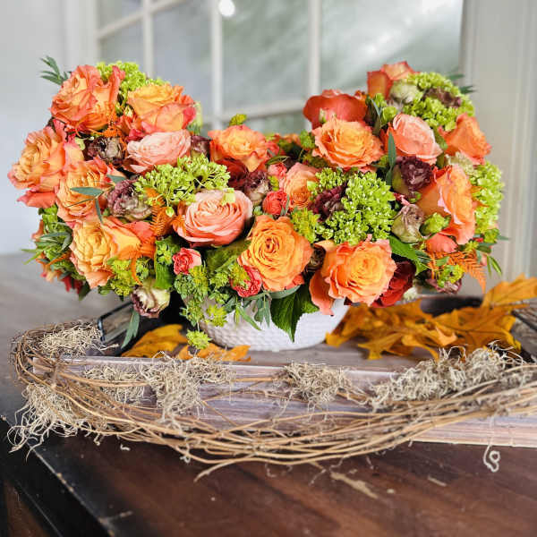 Orange and pink rose arrangement in a white basket on a table