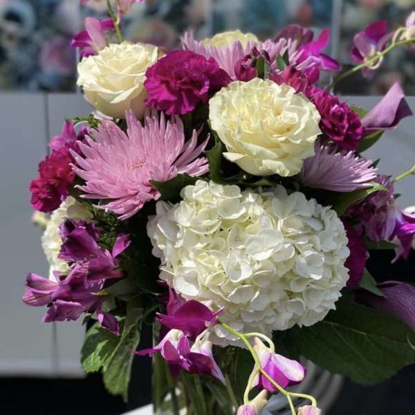 Bouquet of white hydrangeas, pink chrysanthemums, and purple orchids in a glass vase