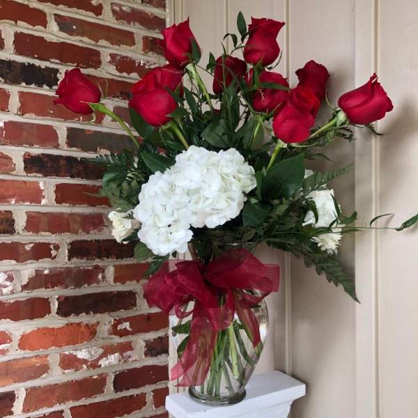 Red roses and white hydrangeas in a clear glass vase with a red ribbon