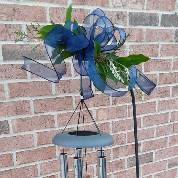 Wind chime with blue ribbon and green leaves on a metal stand