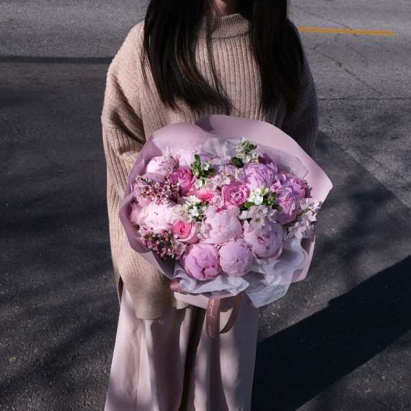 Person holding a pink bouquet of peonies and roses wrapped in pastel paper