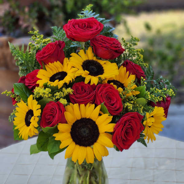 Bouquet of red roses and yellow sunflowers in a glass vase