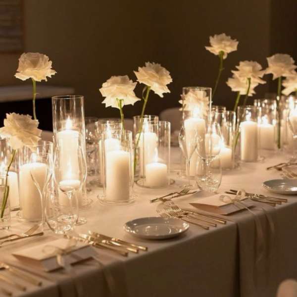 White flowers in glass cylinders with lit candles on a banquet table