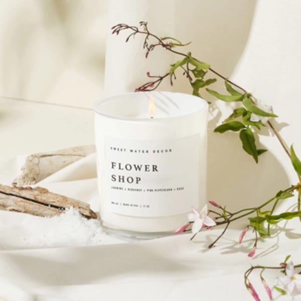 White flower shop candle in a glass jar with a floral sprig beside it