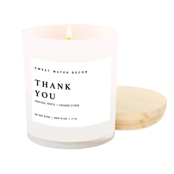 Lit white candle in a glass jar with a lid beside it