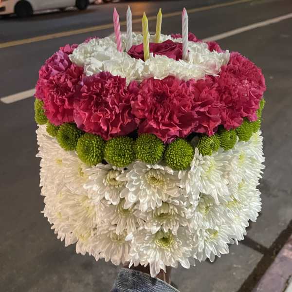 Round floral cake with pink, white, and green flowers and striped candles