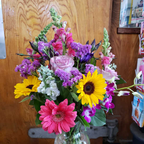 Mixed bouquet in a clear glass vase with pink, yellow, purple, and white flowers