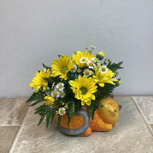 Yellow daisies and white daisies arranged in a cat-shaped ceramic container