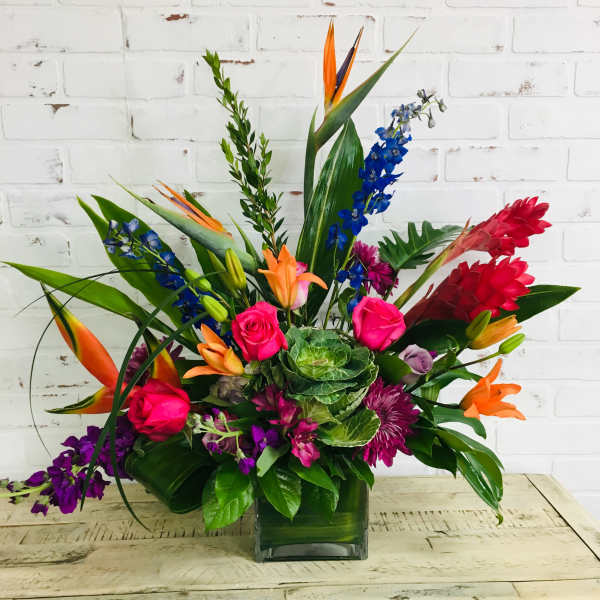 Tropical bouquet with roses, lilies, and blue delphinium in a glass vase