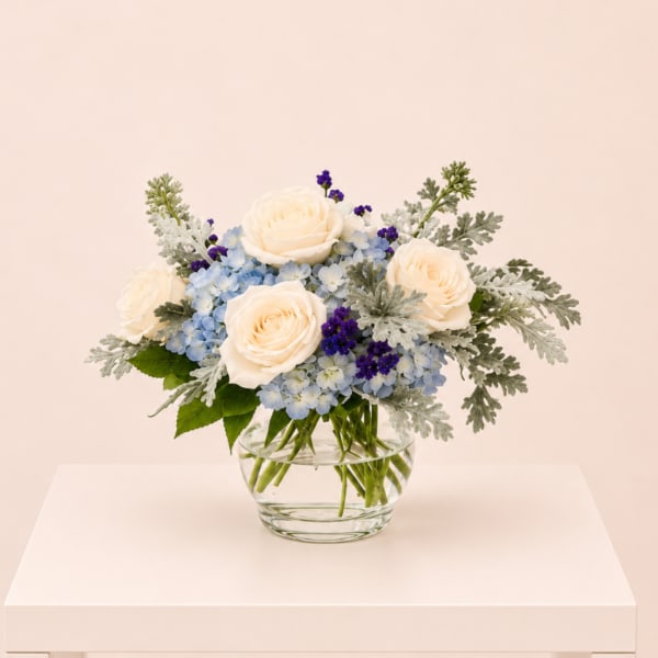 Cream roses and blue flowers in a clear glass vase