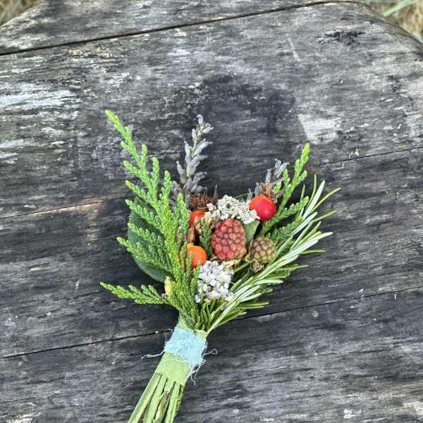 Small boutonniere with berries and greenery tied with blue ribbon